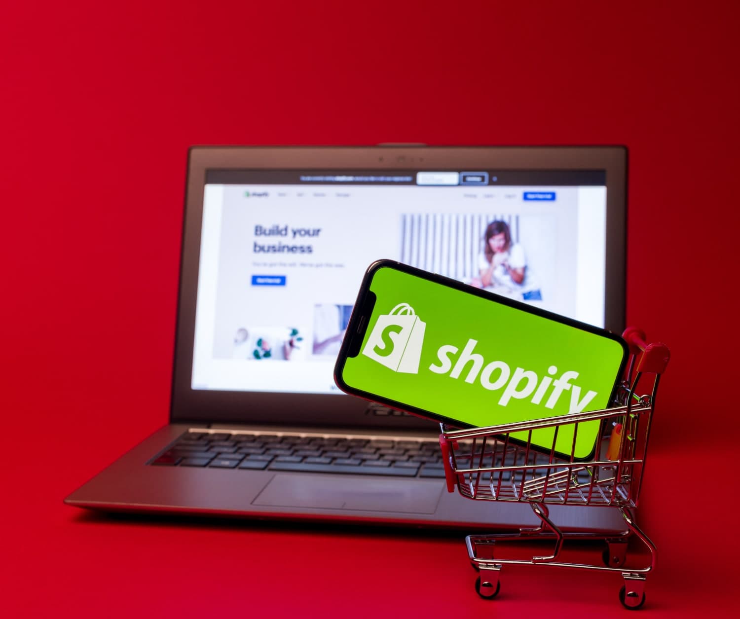 A cellphone with the Shopify logo on the screen in a toy shopping cart